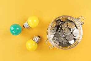 생활 속 에너지 - 노란색 배경지 위에 놓여진 노란색, 초록색 미니 전구들과 유리병에 담겨진 동전들