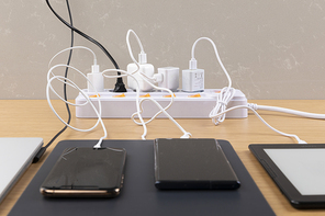 생활 속 에너지 - 나무 배경 위에 놓여진 멀티 탭과 노트북, 스마트폰, 전자책, 태블릿이 연결된 충전기들