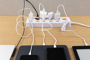생활 속 에너지 - 나무 배경 위에 놓여진 멀티 탭과 노트북, 스마트폰, 전자책, 태블릿이 연결된 충전기들