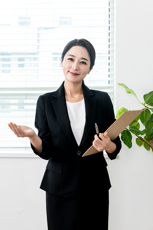 검은색 정장입은 여성이 차트를 들고 안내 손동작 하는 장면 이미지 사진