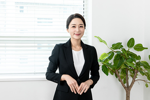 검은색 정장입은 여성이 미소를 지으며 정면 바라보는 장면 이미지 사진