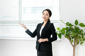검은색 정장입은 여성이 안내 손동작 하며 서있는 장면 이미지 사진