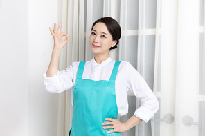 앞치마 입고 있는 여성이 미소 지으며 OK 손동작 하고 있는 이미지 사진
