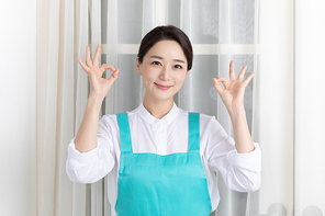 앞치마 입고 있는 여성이 미소 지으며 양손으로 OK 손동작 하고 있는 이미지 사진