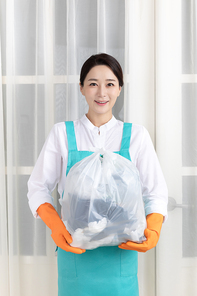 앞치마 입고 있는 여성이 고무장갑 착용하고 쓰레기 봉투 들고 있는 장면 이미지 사진