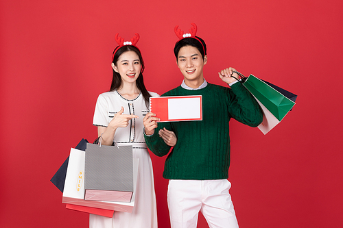 크리스마스 쇼핑이벤트 컨셉 루돌프 머리띠한 커플이 할인쿠폰과 쇼핑백들고 있는 사진 이미지