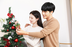 실내에서 크리스마스트리 장식하고 있는 커플
