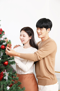 실내에서 크리스마스트리 장식하고 있는 커플