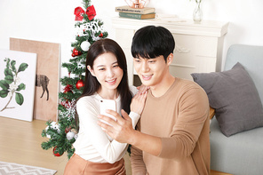 크리스마트트리 배경으로 스마트폰으로 영상통화 하는 커플