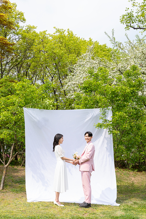 봄커플 스몰웨딩_흰색 배경천에 마주보며 서있는 연인 사진 이미지