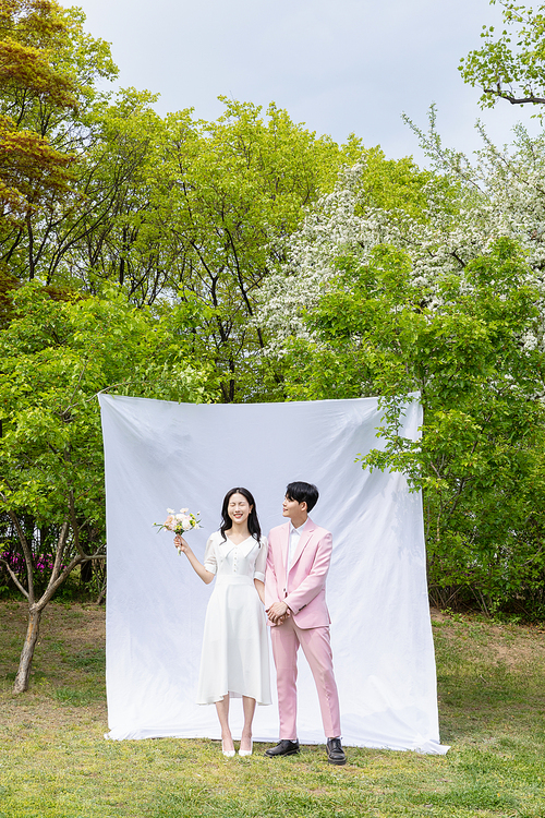 봄커플 스몰웨딩_흰색 배경천에 마주보며 서있는 커플 사진 이미지