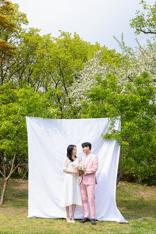 봄커플 스몰웨딩_흰색 배경천에 마주보며 서있는 커플 사진 이미지