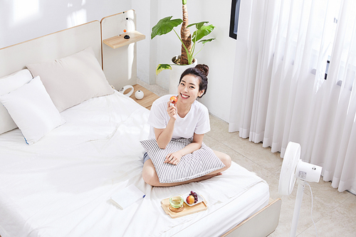 여름일상_침대 위 앉아서 과일을 먹는 여자 사진 이미지