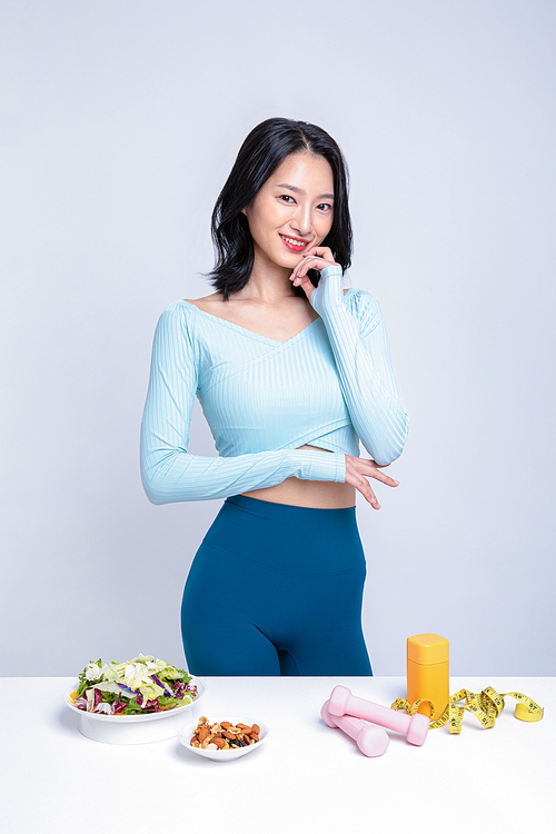 건강한 식사_샐러드 견과류 아령 줄자 알약통 앞에 서있는 운동복을 입은 여성 사진 이미지