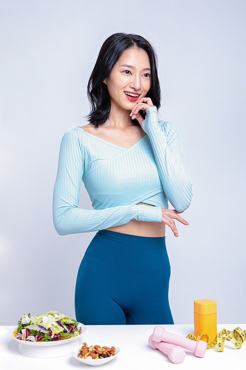 건강한 식사_샐러드 견과류 아령 줄자 알약통 앞에 서있는 운동복을 입은 여성 사진 이미지