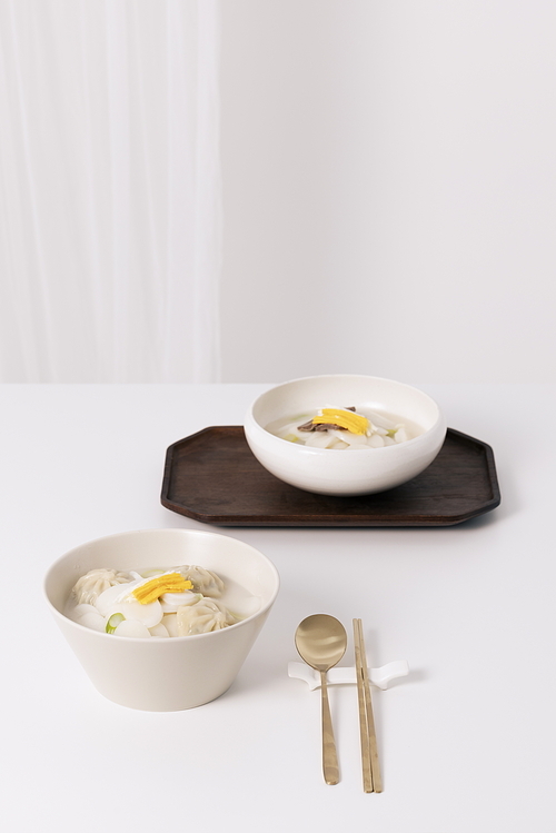 흰탁자위에 떡국 두 그릇과 수저가 놓여있는 사진