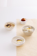 한지가 깔린 흰 식탁위에 떡국 세그릇과 김치가 놓여있는 사진