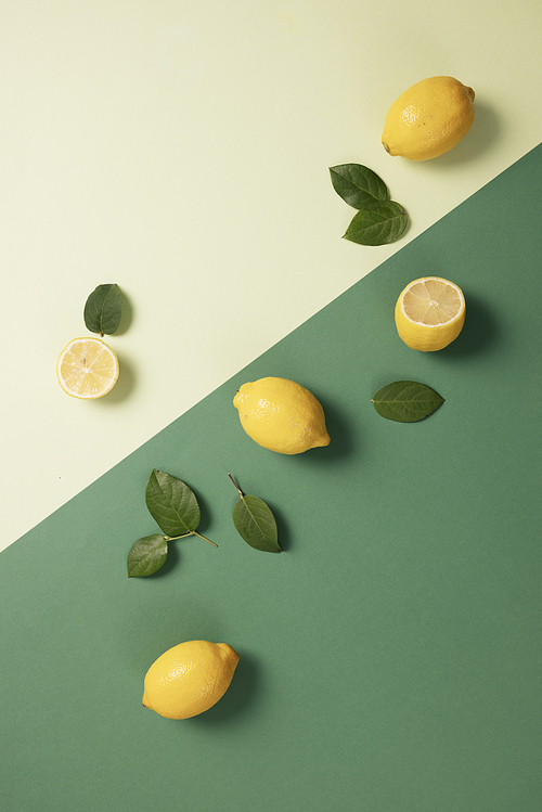 두개의 그린톤 배경에 놓인 노란색 레몬과 초록 잎사귀