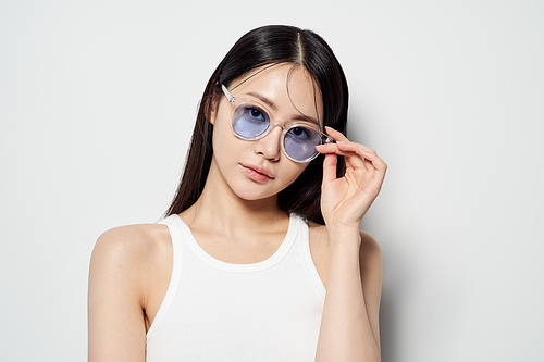 한손으로 투명한 선글라스를 끼고 정면을 응시하는 동양인 여성