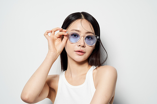 한손으로 투명한 선글라스를 끼고 정면을 응시하는 동양인 여성