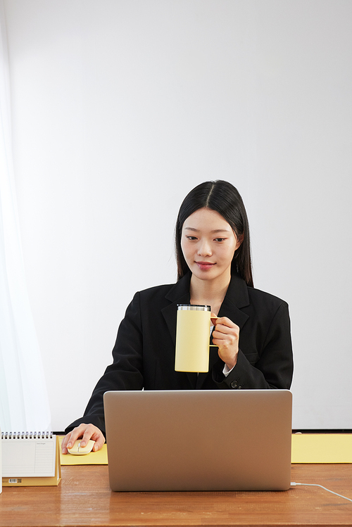 텀블러를 들고 미소지으며 노트북 화면을 보는 여성