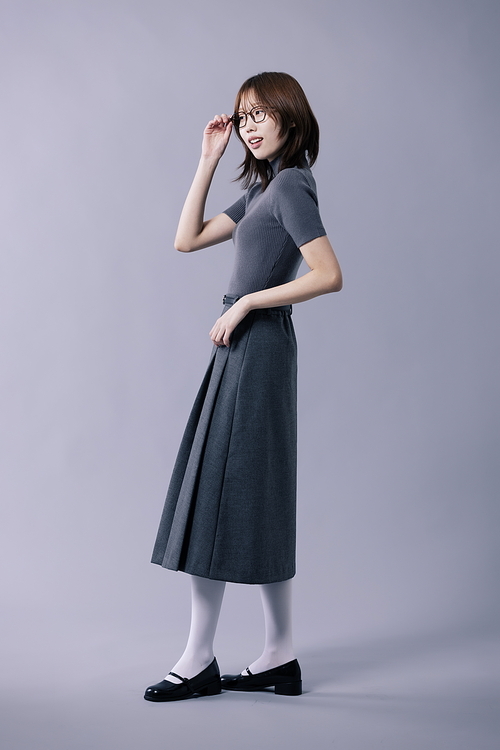 회색 니트 반팔티와 주름스커트를 입고 안경테를 만지는 20대 한국인 여성