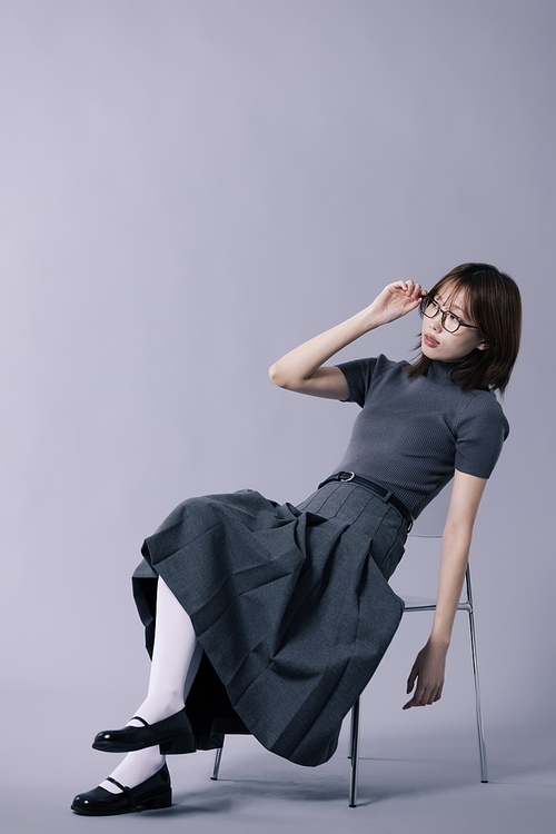 긱시크룩 스타일을 하고 의자에 걸터앉아 안경테를 만지는 20대 한국인 여성