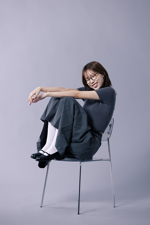 긱시크룩 스타일을 하고 의자에 걸터앉아 눈감고 웃음을 짓는 20대 한국인 여성