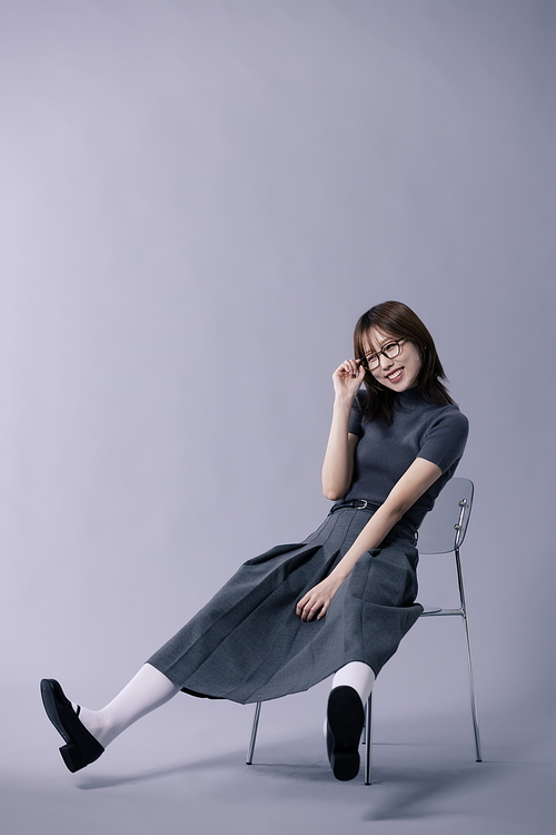 긱시크룩 스타일을 하고 다리를 뻗는채 의자에 앉아 안경테를 만지는 20대 한국인 여성