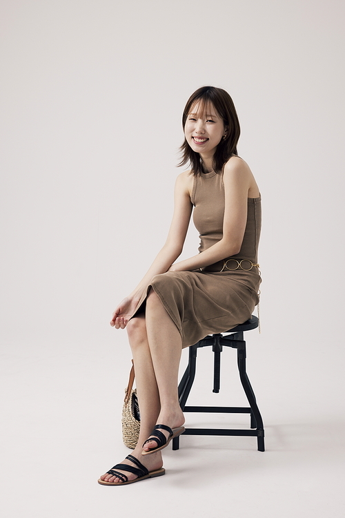 의자에 앉아 다리를 꼬고 밝은 표정을 짓는 한국인 여성