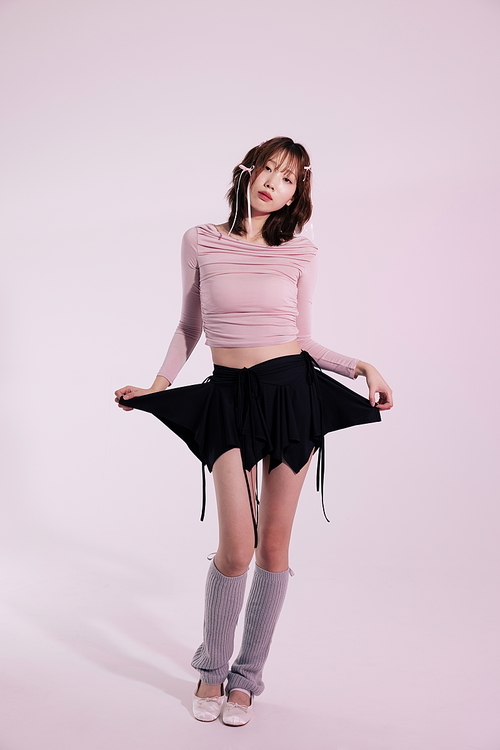 발레코어룩 스타일을 착장하고 검은색 스커트를 만지며 포즈를 취하는 20대 한국인 여성
