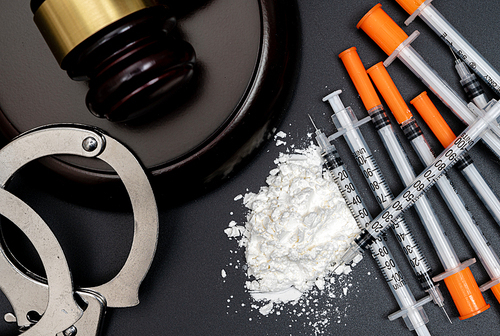 검은 배경에 흰색 가루와 주사기 그리고 의사봉이 있는 마약 범죄 컨셉