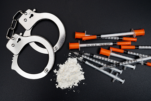 검은 배경에 흰색 가루와 주사기 그리고 수갑이 있는 마약 범죄 컨셉
