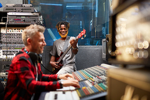 African musician playing guitar while producer recording him in studio