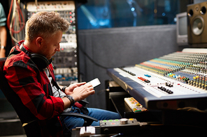 Modern dj sitting in studio and reading short messages from radio listeners during music break