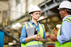 Two manual workers wearing hardhats, vests and safety glasses