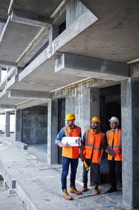Inspectors in helmets and uniform standing by unfinished construction