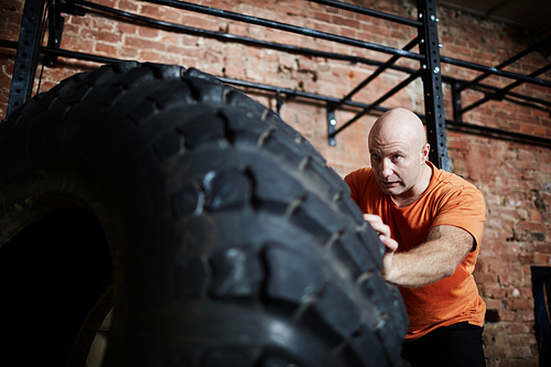 Sportsman in T-shirt flipping tire in gym