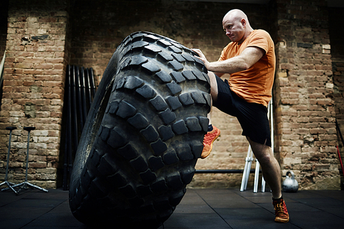Young bald man in sportswear exercising with tire