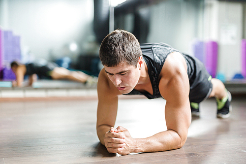 Muscular young man doing planks on the floor of gym