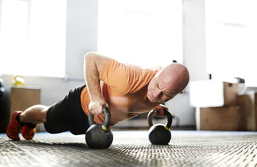 Muscular athlete pushing up with kettlebells