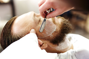 Close-up of young man having his beard shaven