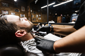 Stubbled man relaxing in barbershop during shaving procedure