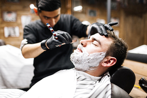 Young man wit hfoam on his face having his bristle shaven