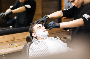 Barber using sharp razor for shaving bearded man