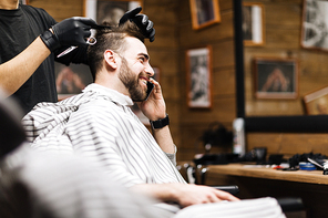 Happy businessman speaking on mobile phone during haircut