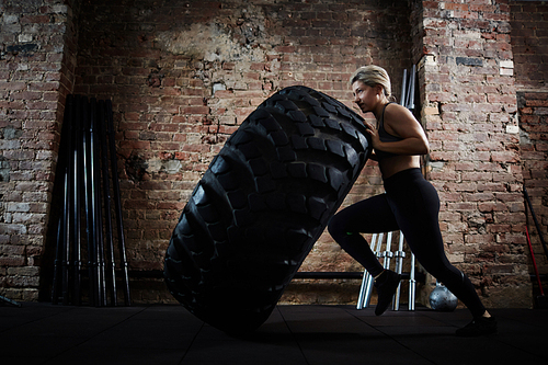 Woman in activewear making effort while flipping tire