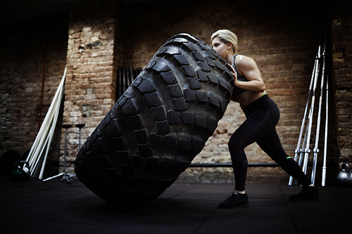 Young strong female in activewear flipping heavy tire