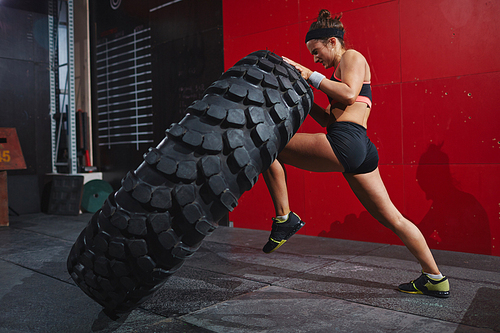 Active woman in sportswear flipping tyre in gym