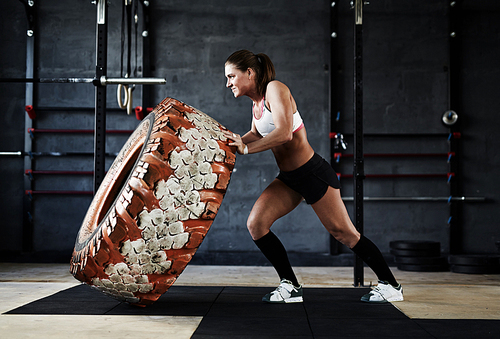 Active and strong woman flipping tyre in gym